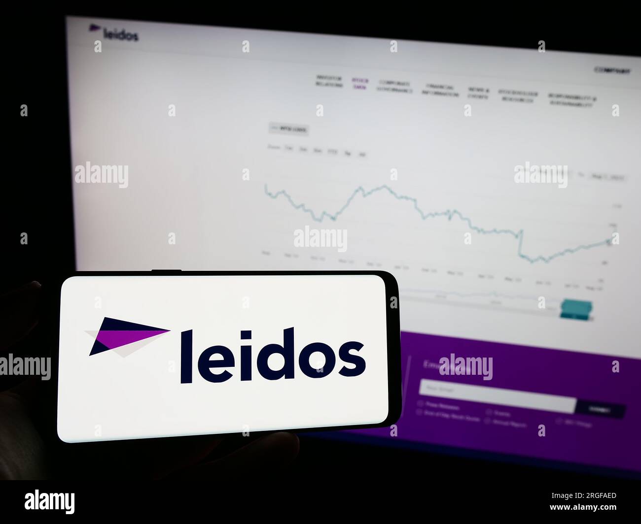 Person holding mobile phone with logo of American defense company Leidos Inc. on screen in front of business web page. Focus on phone display. Stock Photo