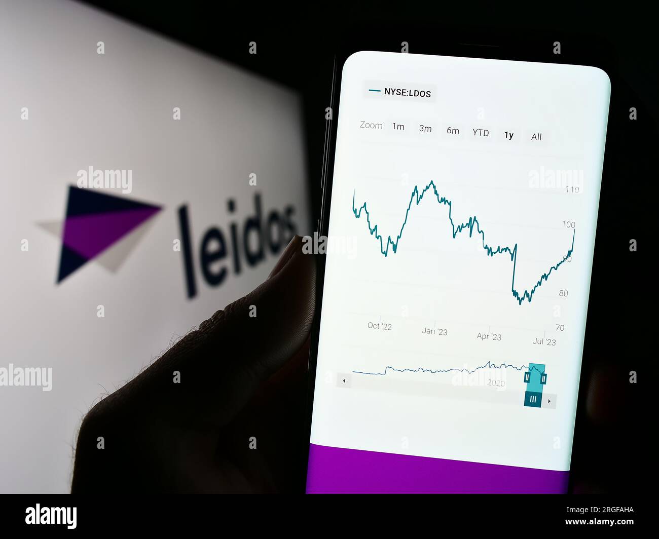 Person holding cellphone with website of US defense company Leidos Inc. on screen in front of business logo. Focus on top-left of phone display. Stock Photo