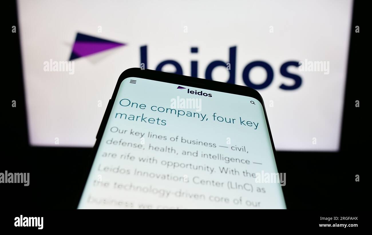 Mobile phone with webpage of US defense company Leidos Inc. on screen in front of business logo. Focus on top-left of phone display. Stock Photo