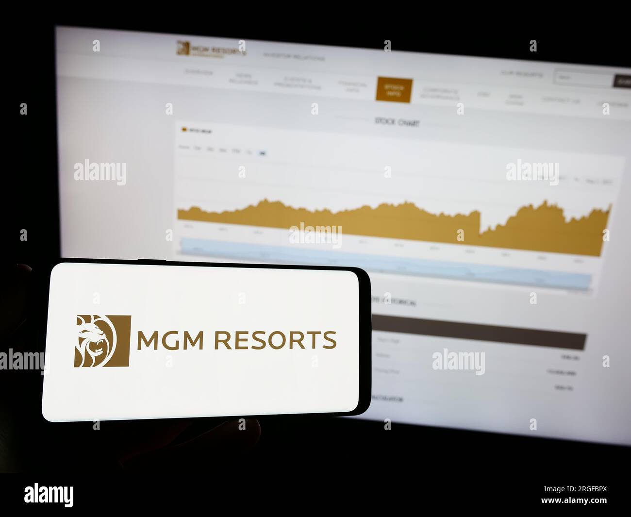 Person holding mobile phone with logo of hospitality company MGM Resorts International on screen in front of web page. Focus on phone display. Stock Photo