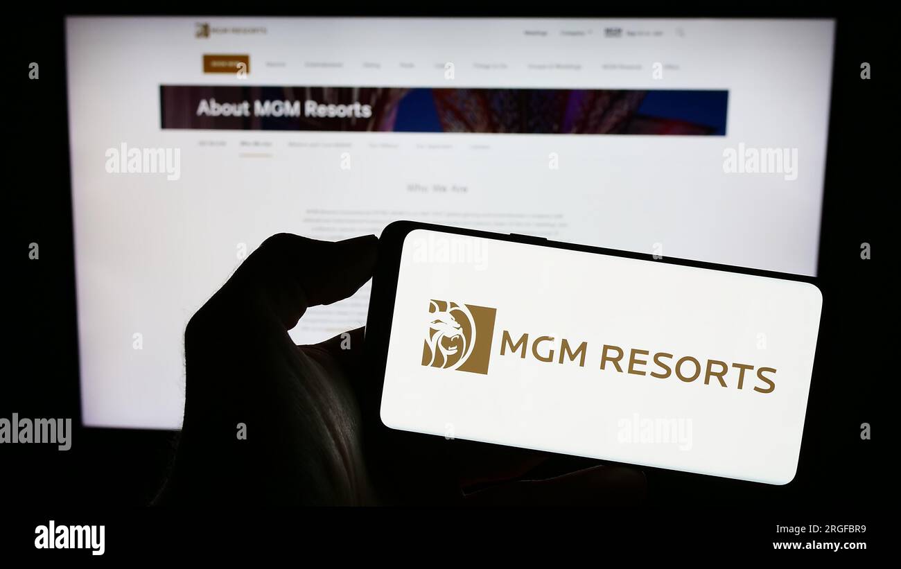 Person holding smartphone with logo of hospitality company MGM Resorts International on screen in front of website. Focus on phone display. Stock Photo