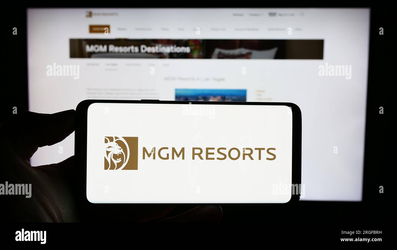 Person holding cellphone with logo of US hospitality company MGM Resorts International on screen in front of webpage. Focus on phone display. Stock Photo
