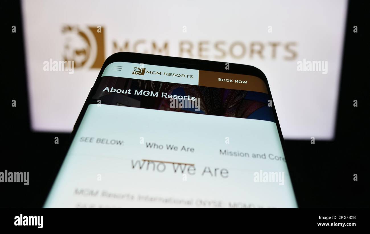 Mobile phone with webpage of hospitality company MGM Resorts International on screen in front of logo. Focus on top-left of phone display. Stock Photo
