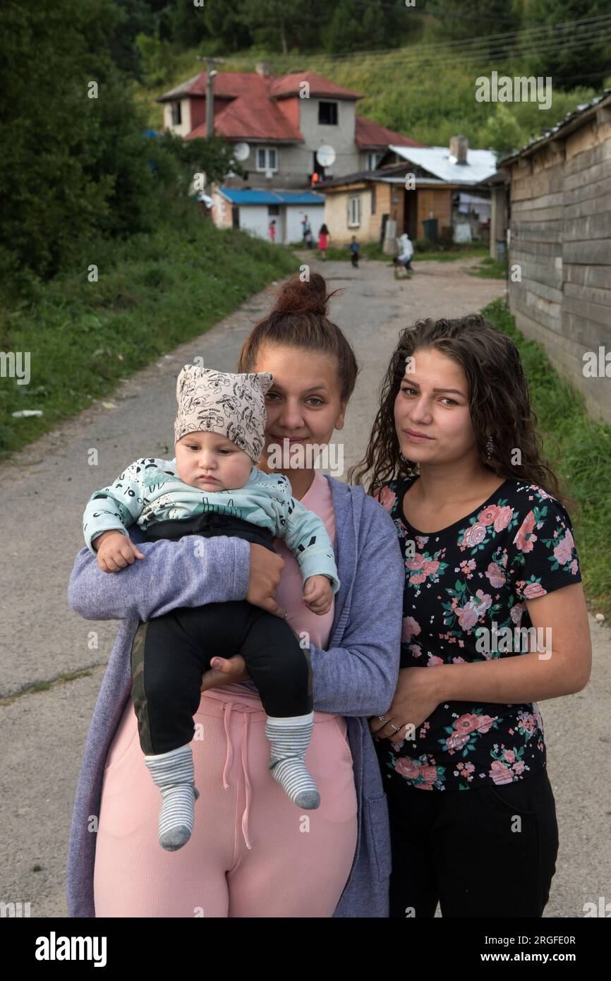 Romany gypsy young mother with her baby and friend. Multi generational house in background. Gypsy settlement on the outskirts of Sumiac, Brezno District, Slovakia August 2023. 2020s HOMER SYKES Stock Photo