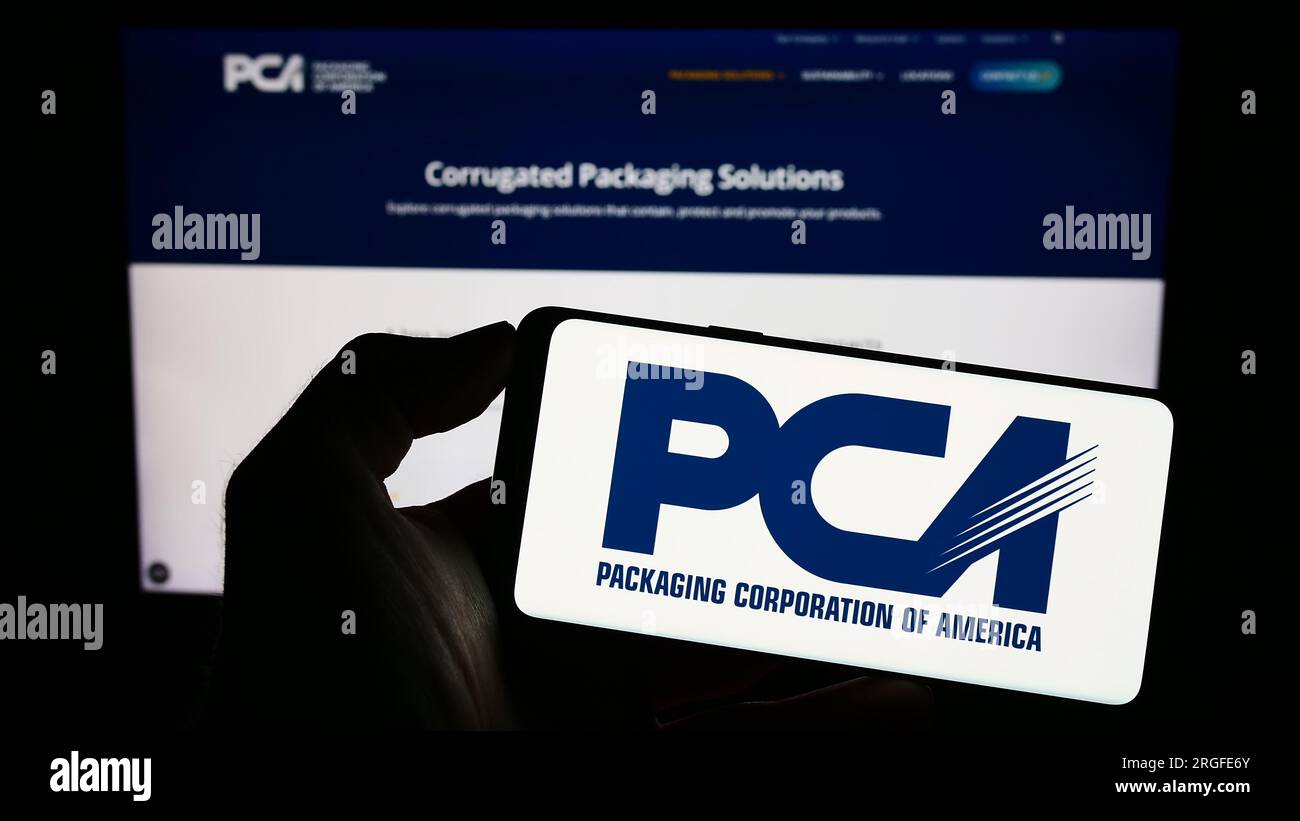 Person holding cellphone with logo of US company Packaging Corporation of America (PCA) on screen in front of web page. Focus on phone display. Stock Photo