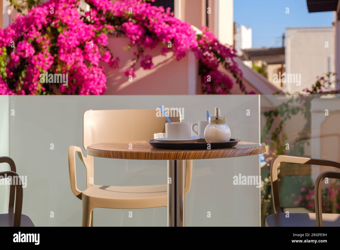 View of two coffee mugs and a sugar shaker on a table surrounded by chairs at a balcony in Fira Santorini Greece Stock Photo