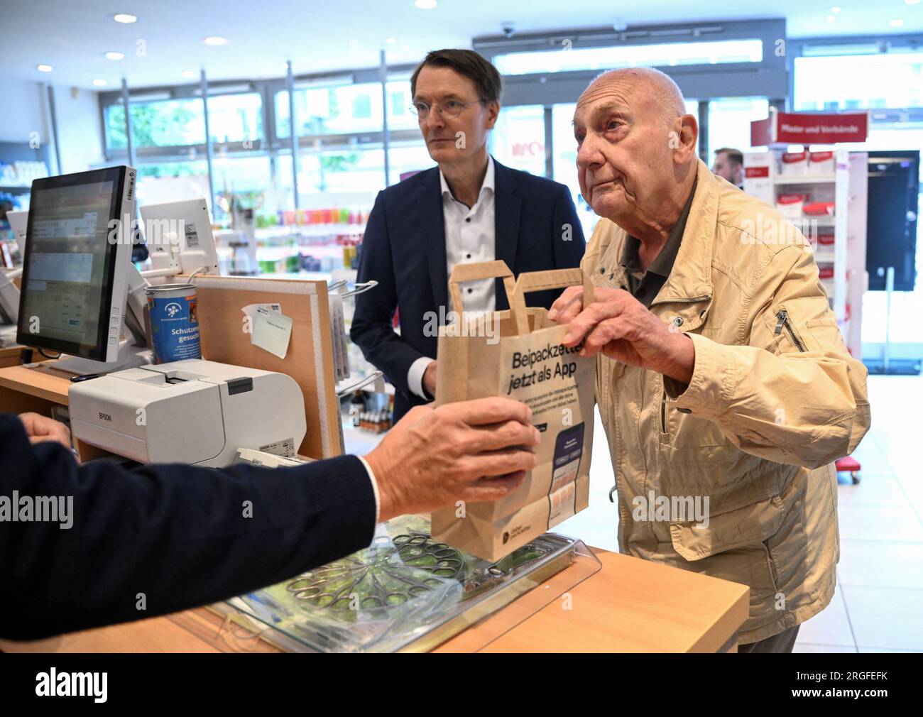 09 August 2023, Berlin: Peter Jordan (86) buys medicines in a pharmacy, next to him stands Federal Health Minister Karl Lauterbach (l, SPD) who is presenting the new procedure for issuing an electronic prescription. Photo: Annegret Hilse/Reuters/Pool/dpa Stock Photo