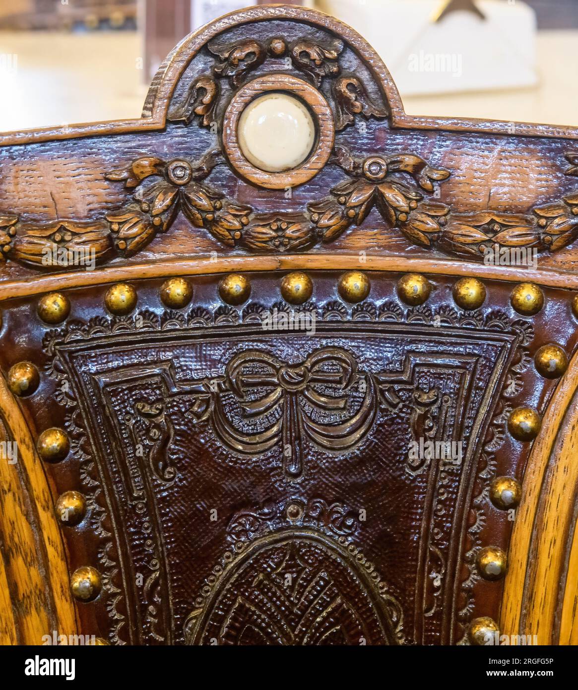 Ancient seat back. The wooden part has decorative carvings. The leather is supported with rivets and has engraved ornaments. Stock Photo