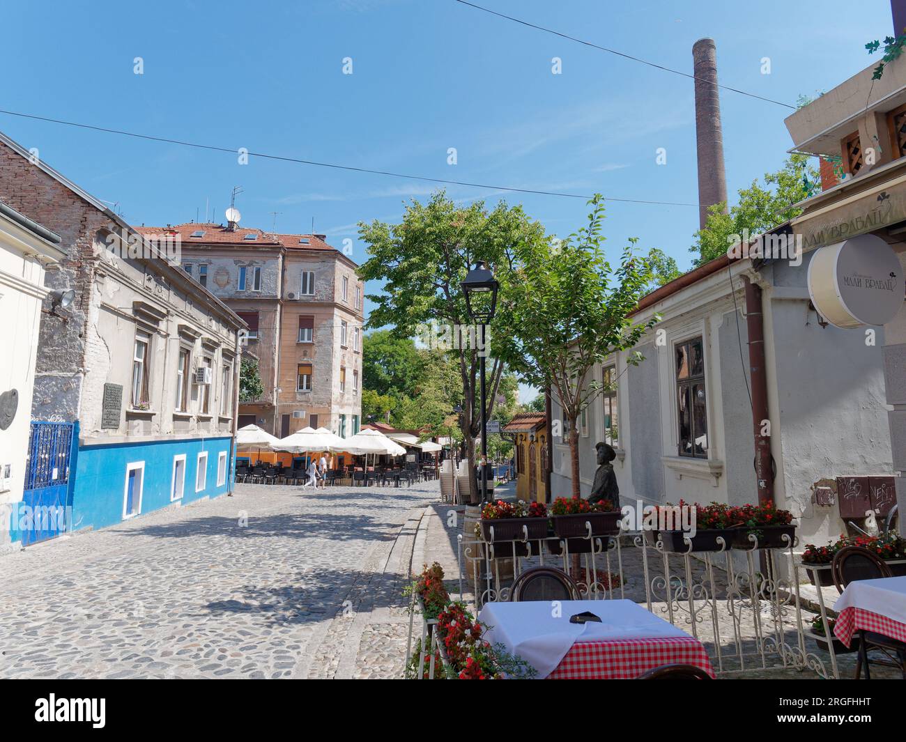 The famous bohemian cobbled Skadarlija street with cafes and restaurants and the statue of poet Đura Jaksic right. Belgrade, Serbia. August 9, 2023.. Stock Photo