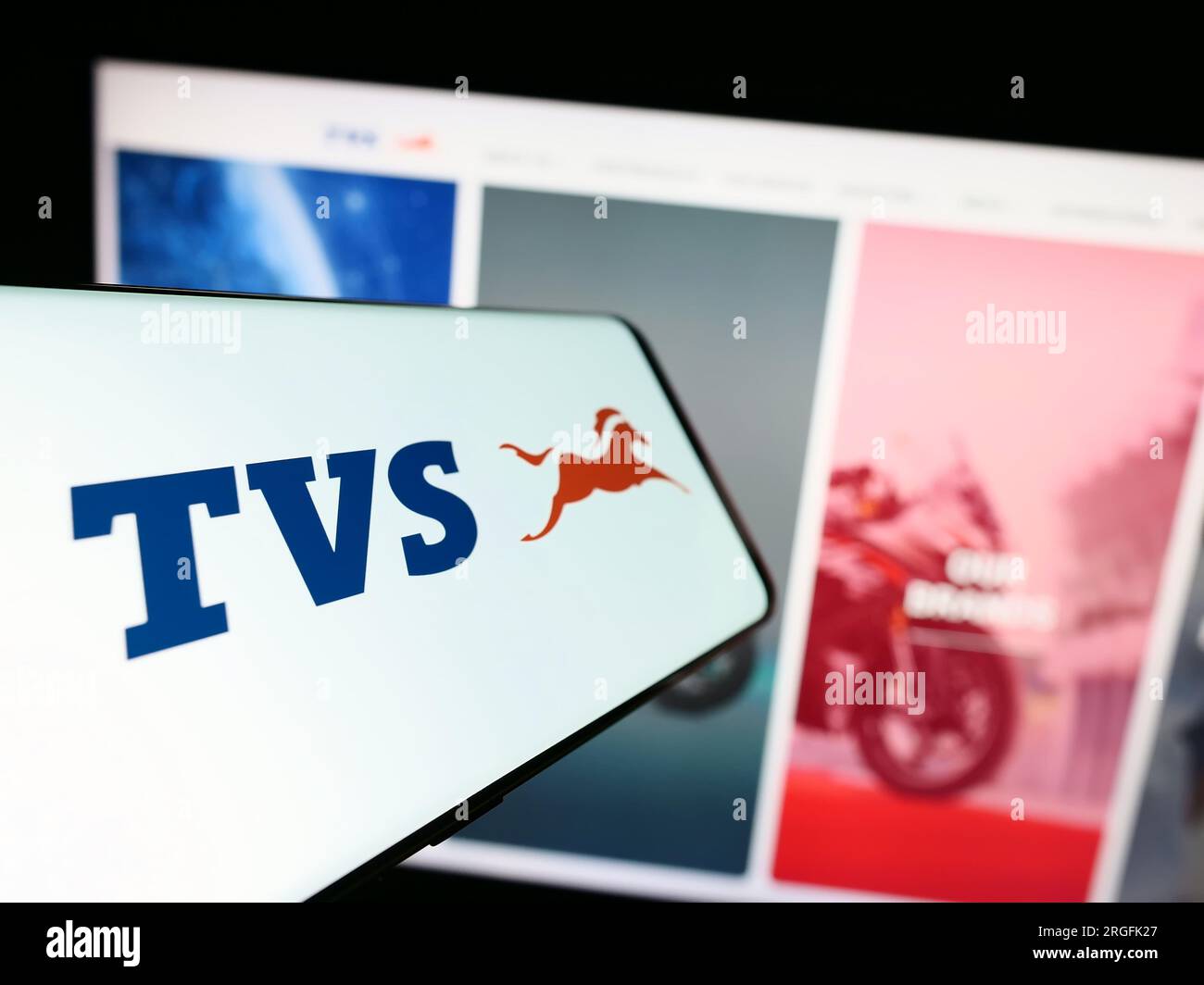 Smartphone with logo of motorcycle company TVS Motor Company Limited on screen in front of website. Focus on center-left of phone display. Stock Photo