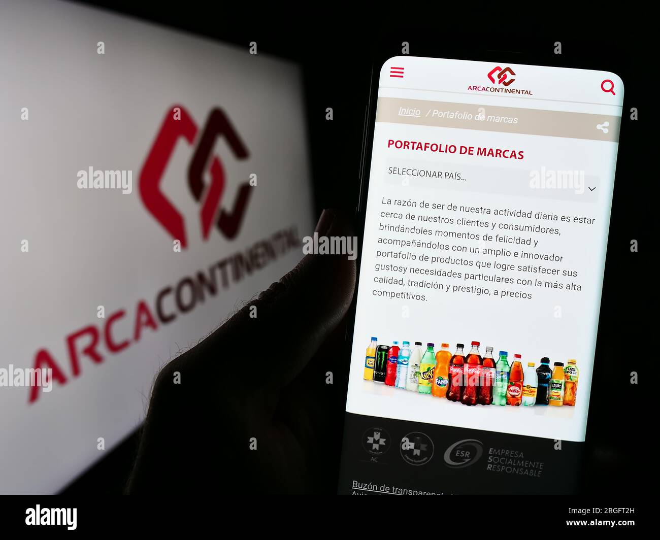 Person holding cellphone with webpage of company Arca Continental S.A.B. de C.V. on screen in front of logo. Focus on center of phone display. Stock Photo