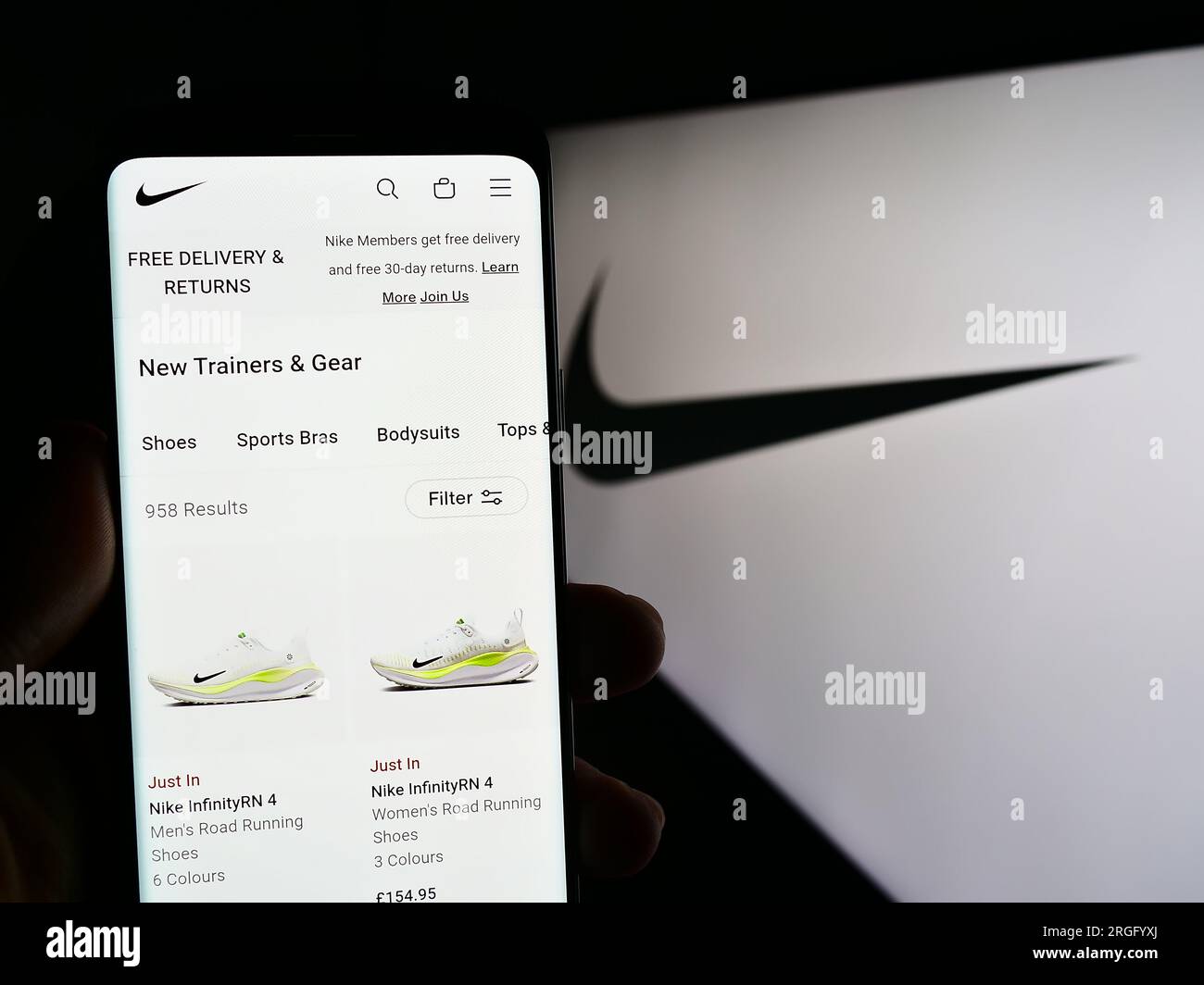 Person holding cellphone with web page of American sportswear company Nike Inc. on screen in front of logo. Focus on center of phone display. Stock Photo