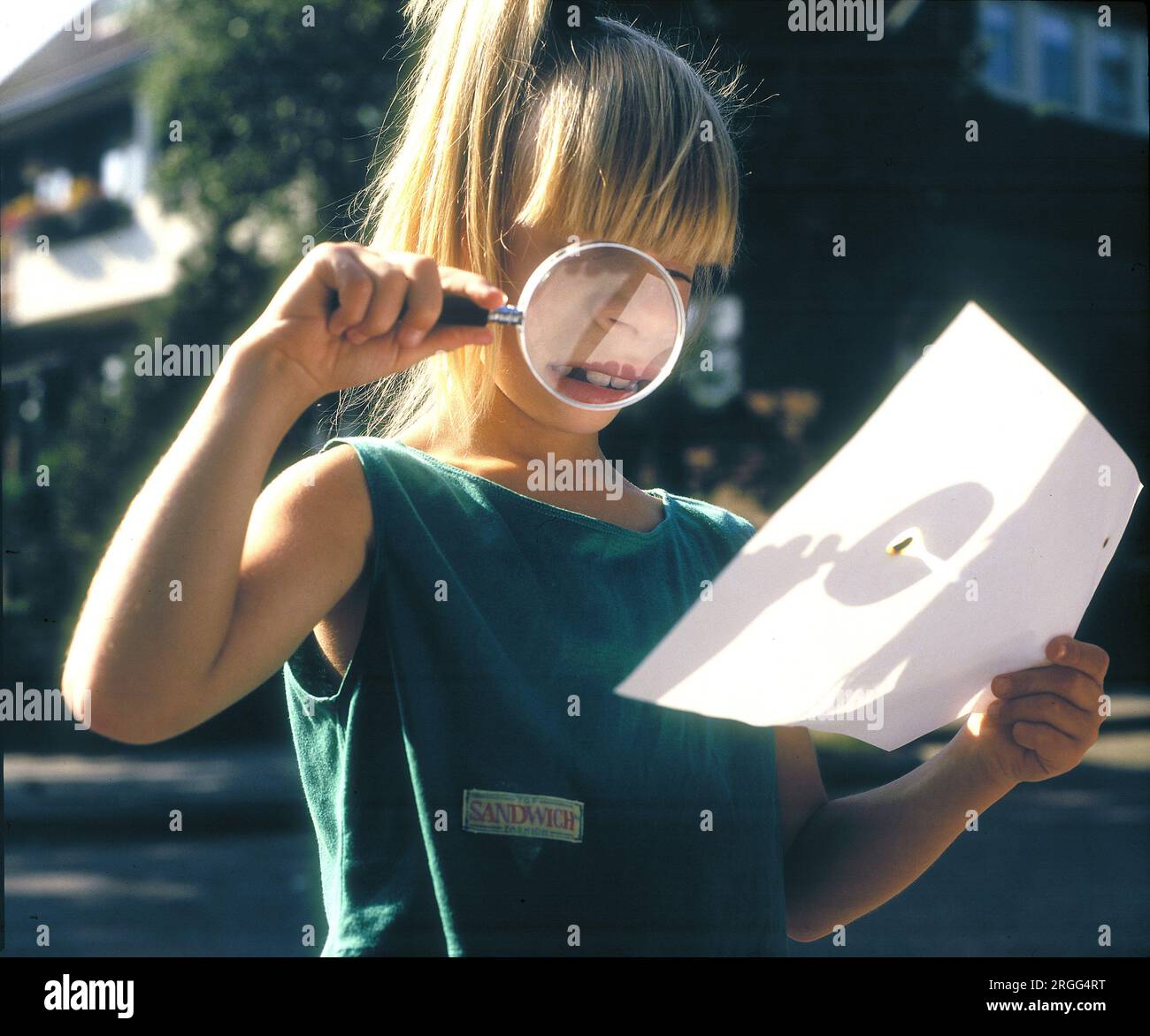 Girl burning a hole in a piece of paper using a magnifying glass. Netherlands Stock Photo