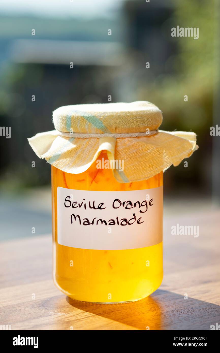 A jar containing home made Seville orange marmalade. The jar has a hand written label and a fabric topping over the lid Stock Photo