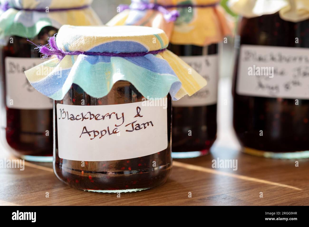 Jars of homemade Blackberry and apple jam. the jars have clear handwritten lables and the jars have a cloth topping Stock Photo