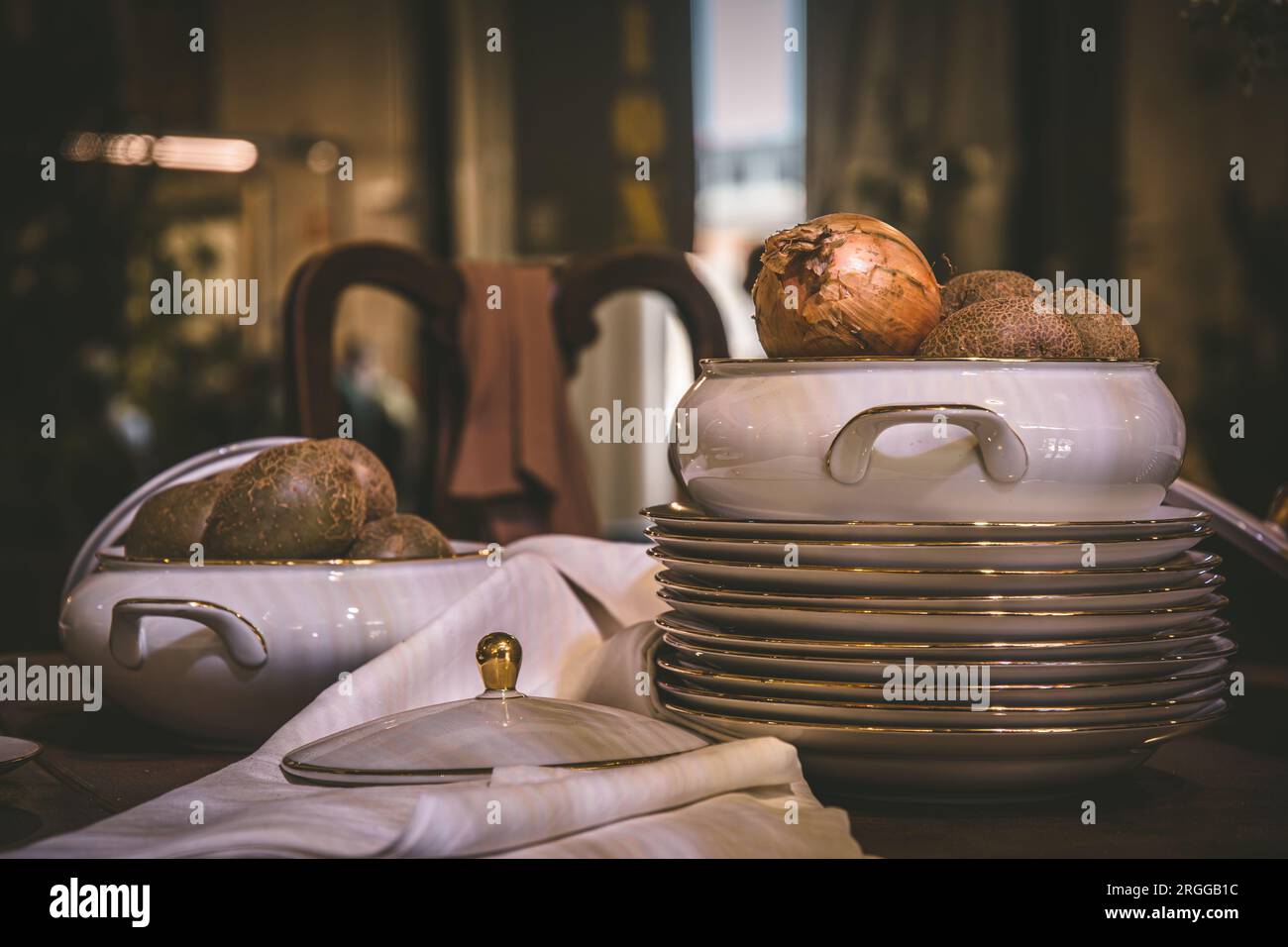 Stacked plates with gold rim and bowl with onions on an old wooden table Stock Photo