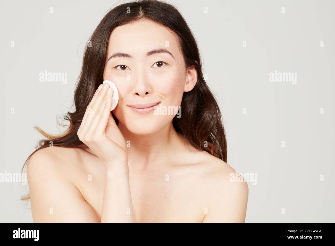 Young woman wiping face with cotton pad Stock Photo