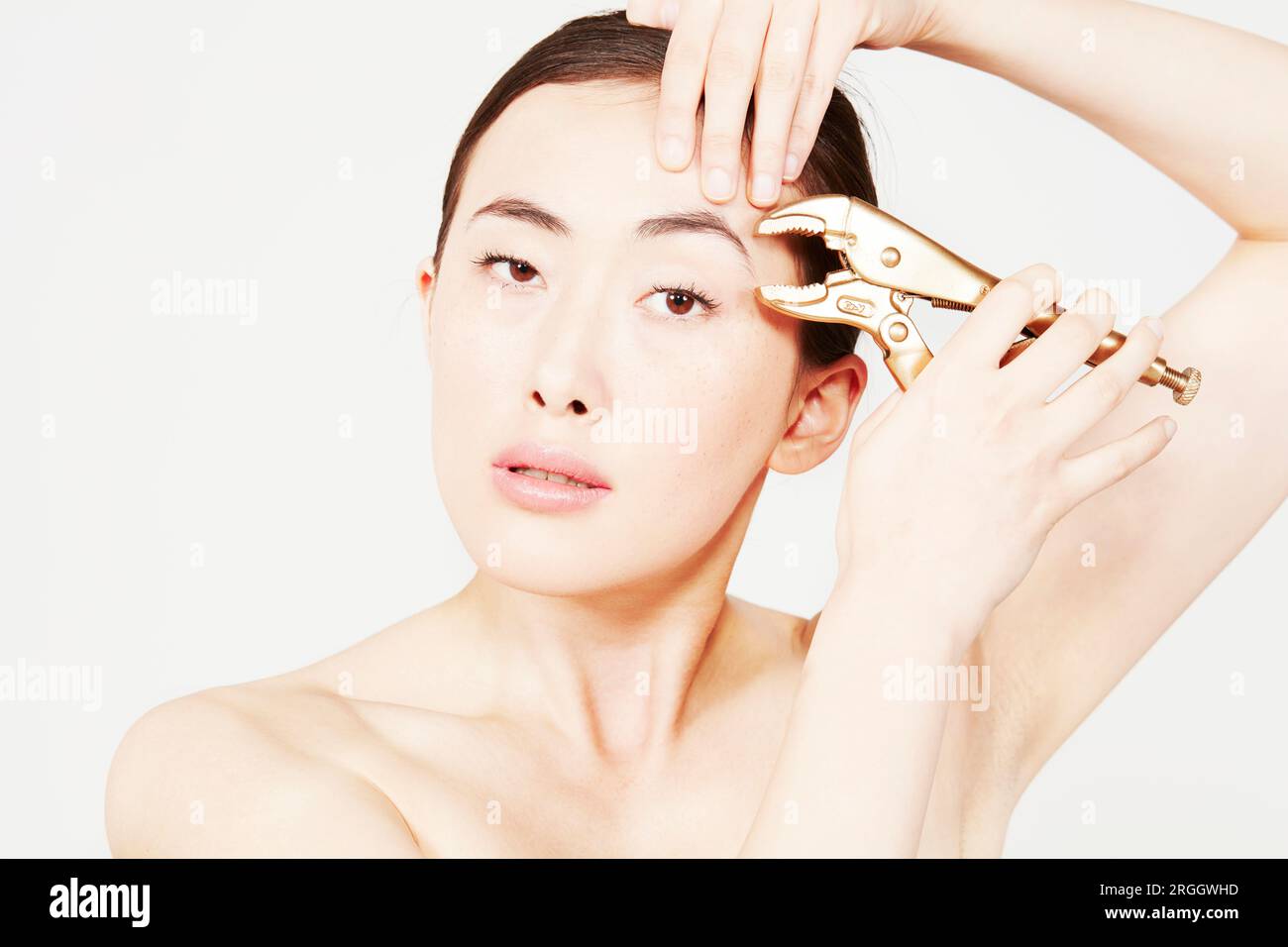 Young woman using locking pliers on eyebrows Stock Photo