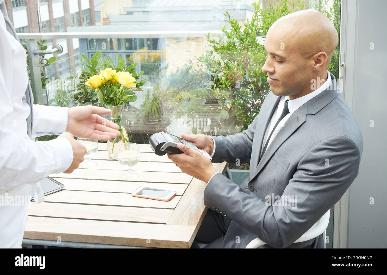 Businessman using EFTPOS machine at restaurant table Stock Photo