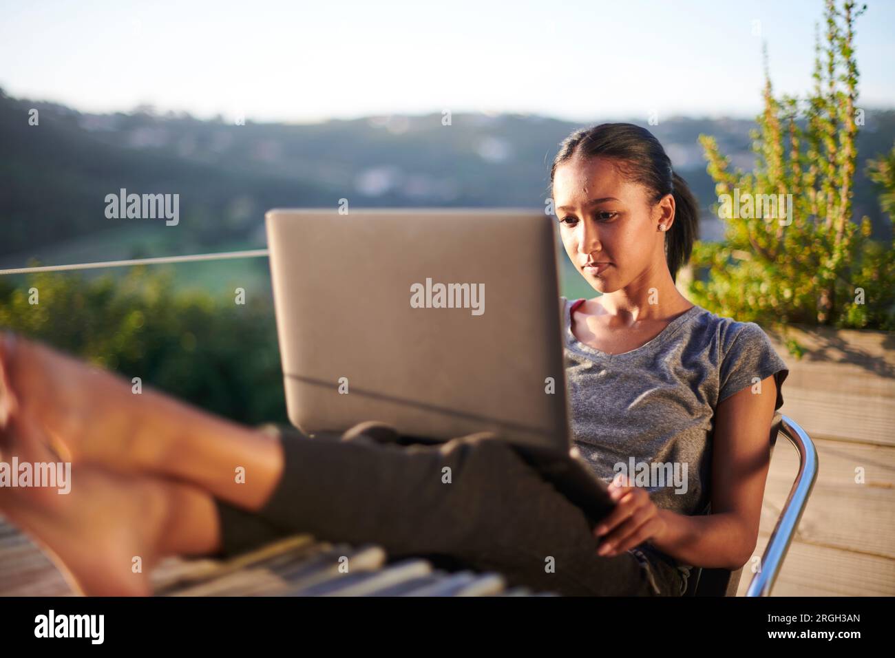 https://c8.alamy.com/comp/2RGH3AN/young-woman-using-laptop-on-balcony-at-sunset-2RGH3AN.jpg