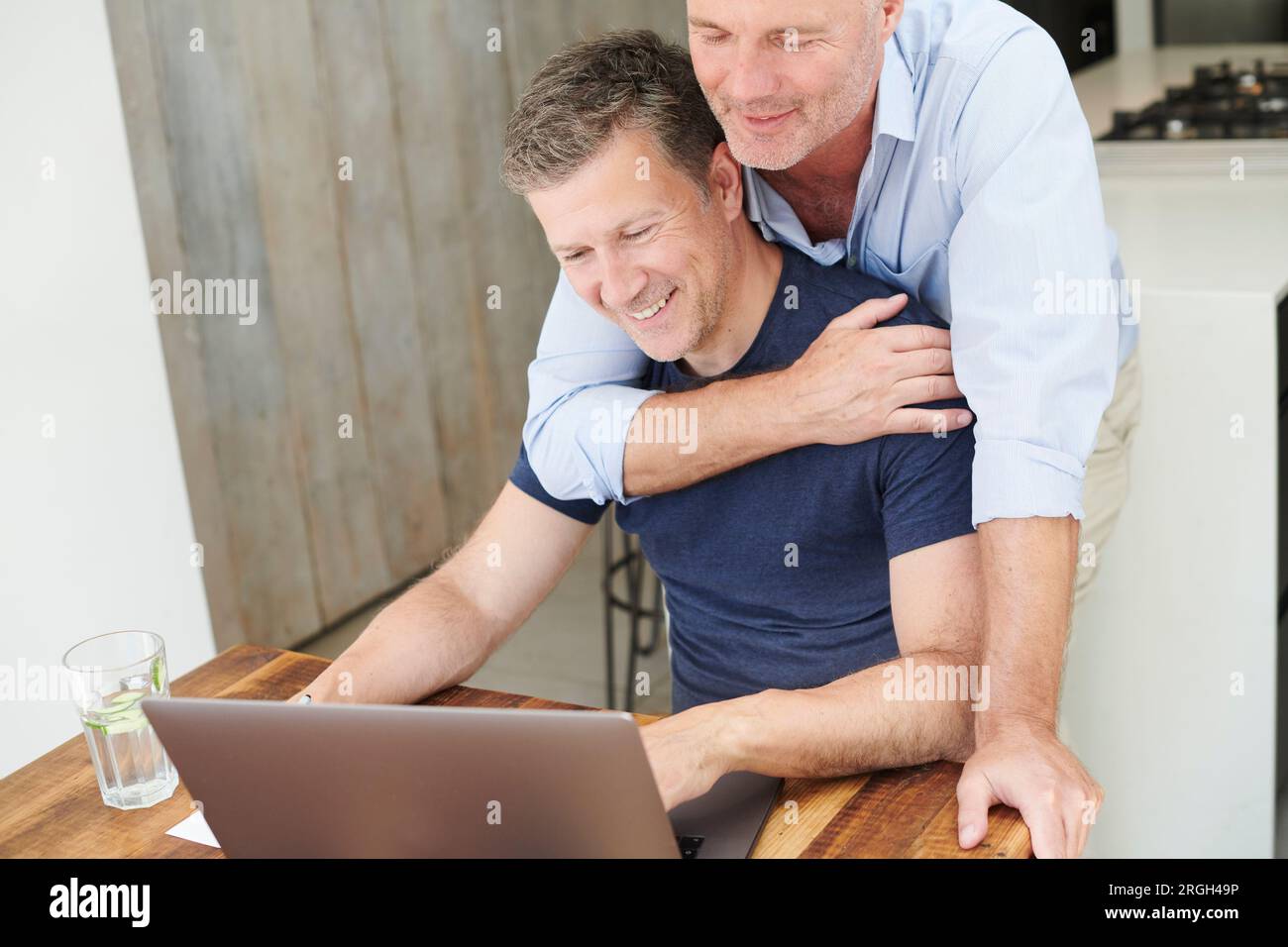 Gay couple embracing while using laptop Stock Photo