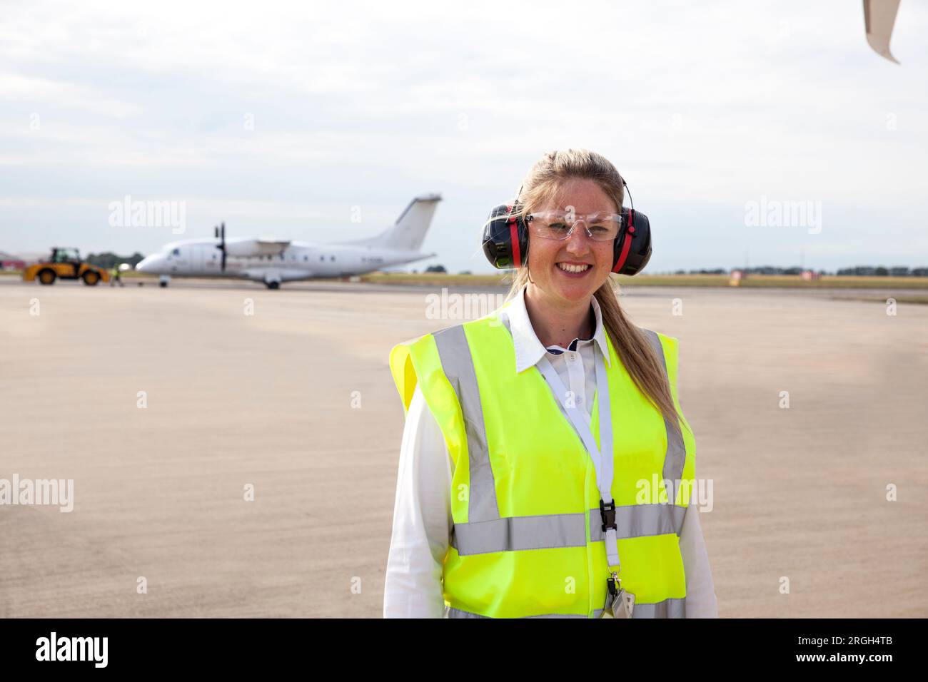 Smiling worker wearing ear muffs on airplane runway Stock Photo