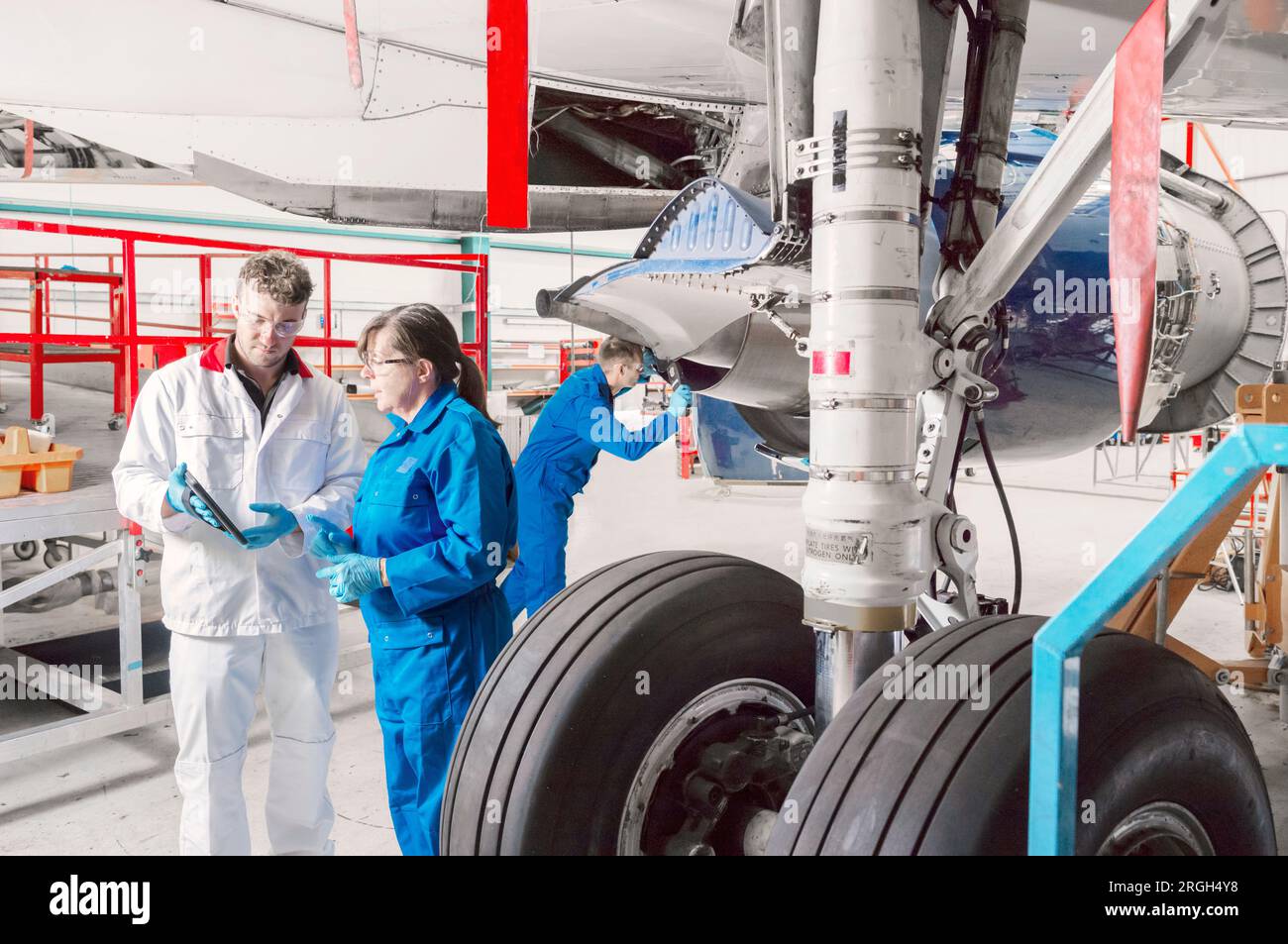 Workers using digital tablet by airplane wheels in hangar Stock Photo