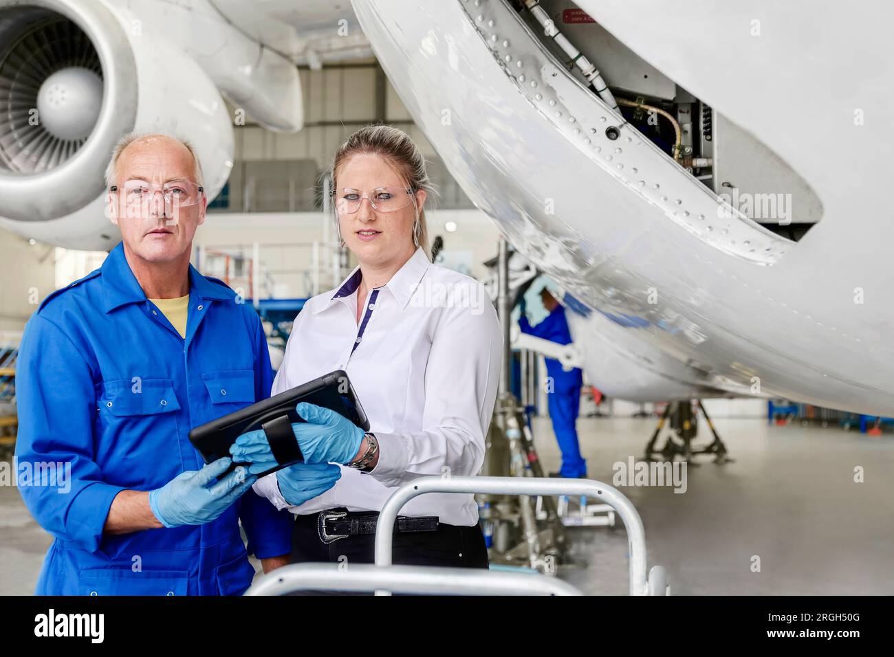 Workers using digital tablet by airplane in hangar Stock Photo