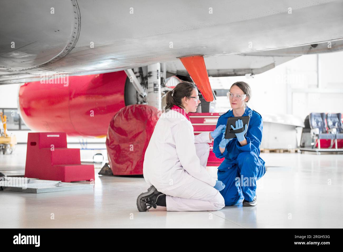 Crouched women using digital tablet under airplane Stock Photo