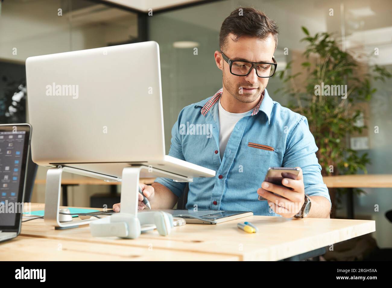 Young man holding smart phone by laptop Stock Photo