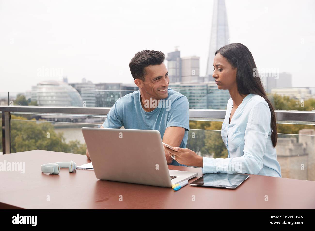 Colleagues using laptop on balcony Stock Photo