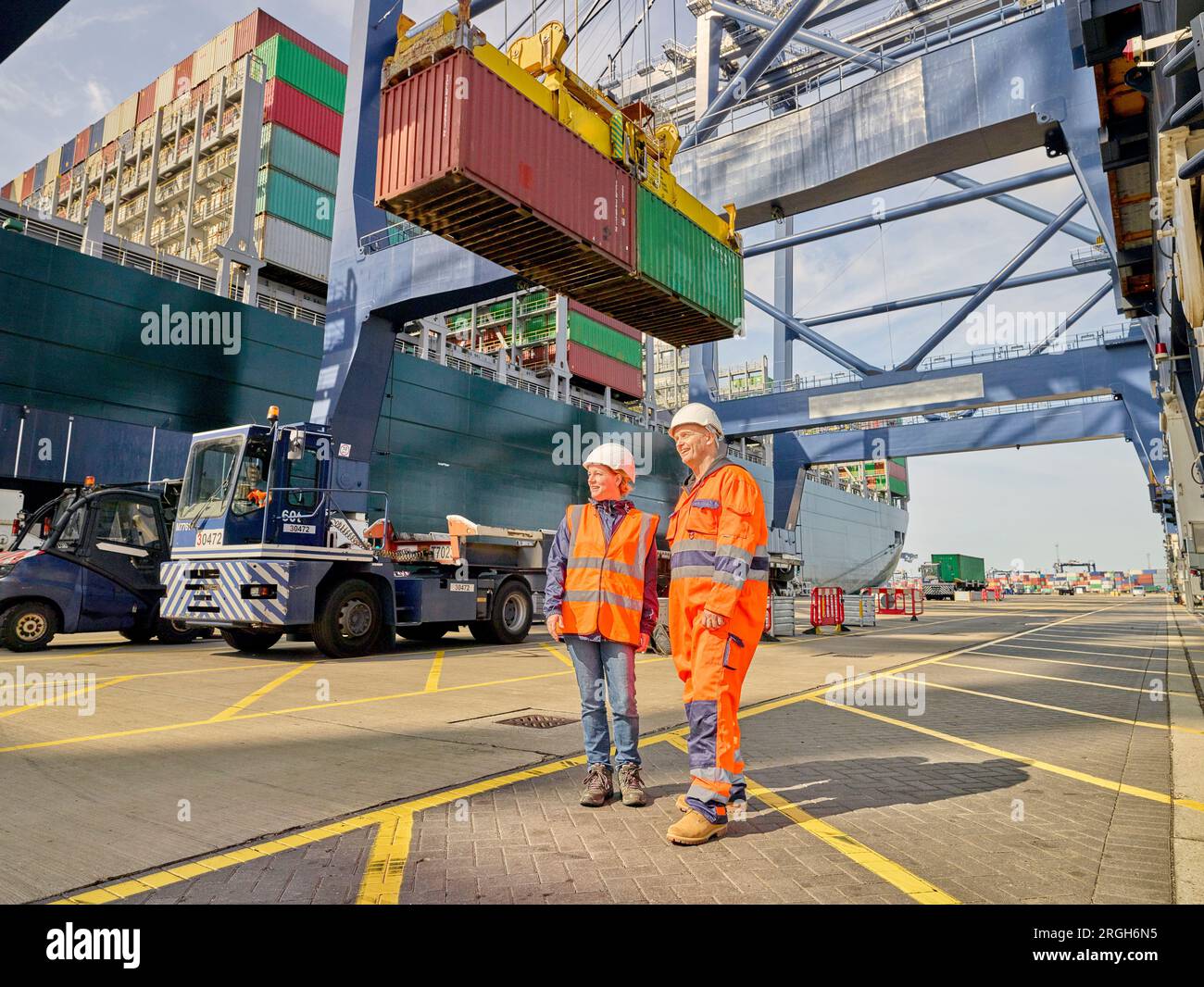 Dock workers by crane lowering cargo container onto truck Stock Photo