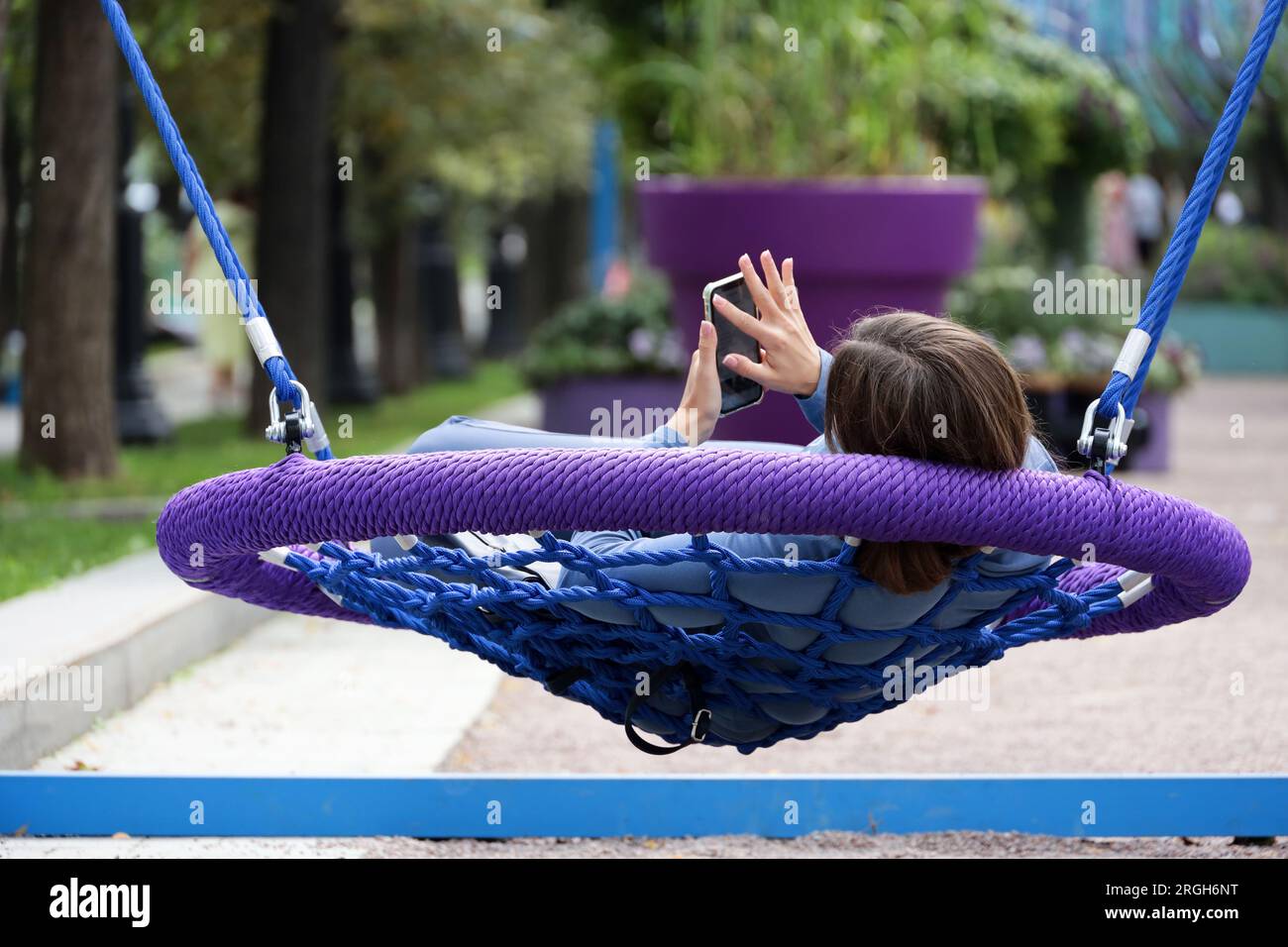 Girl lying with smartphone in swing, leisure in summer park Stock Photo