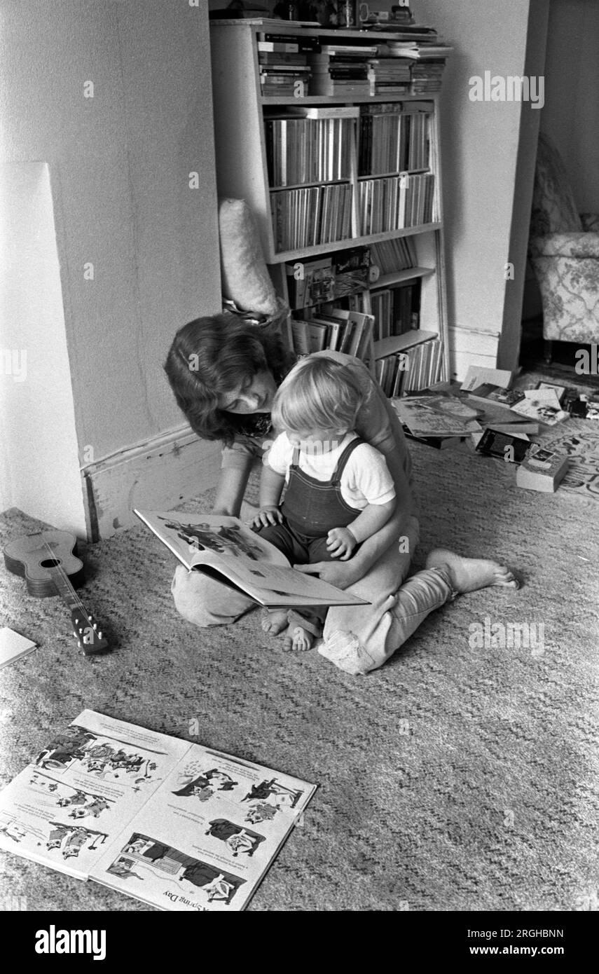Family life interior home 1970s UK. Mother reading book to baby son sitting on the floor learning to read. Mum spending quality time together with first child. Interior of living room middle class family life 1970s 1975 Southfields, South London UK HOMER SYKES Stock Photo