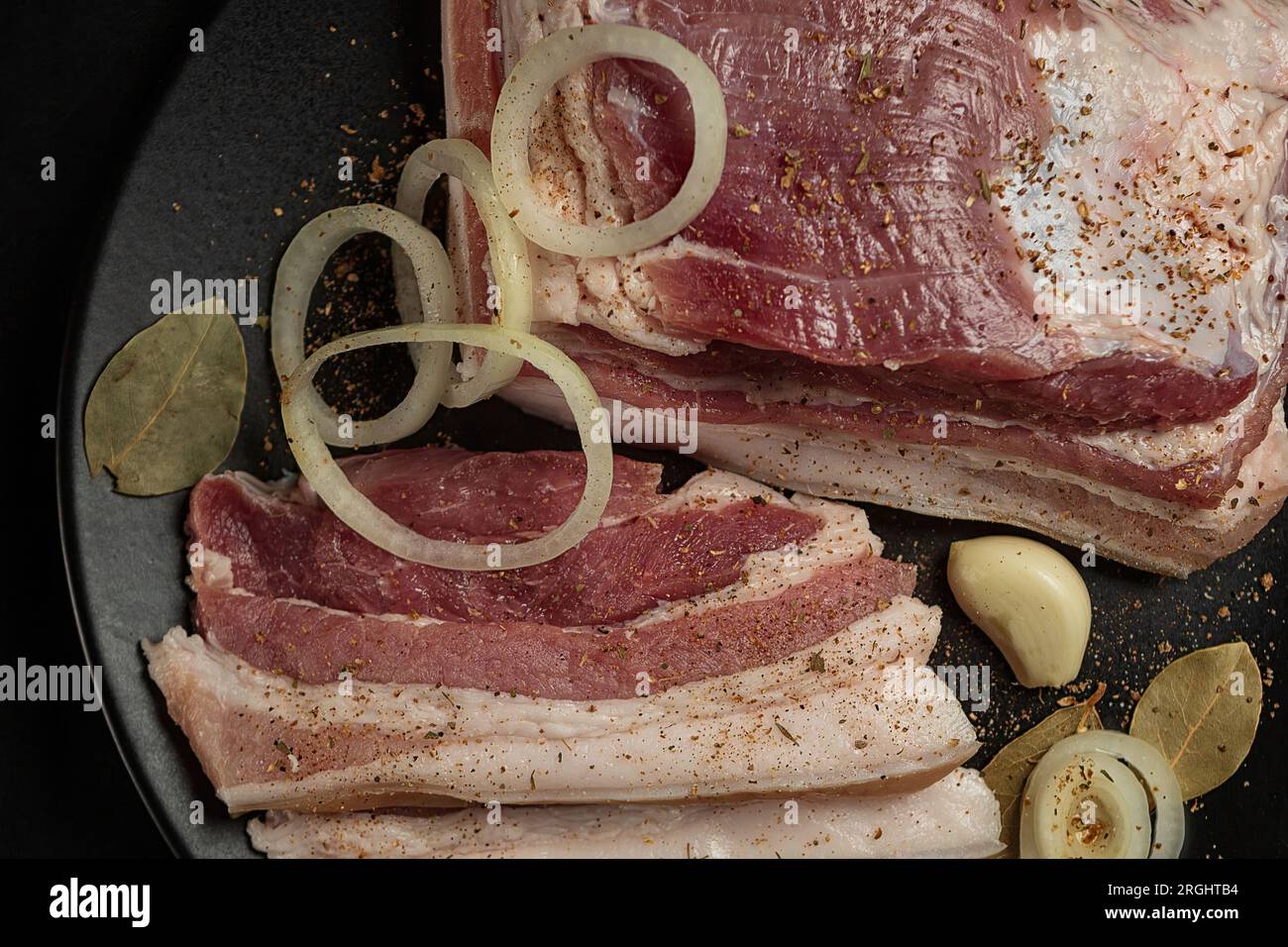 Raw pork thigh, knuckle, ham with spices and onions, on a black plate