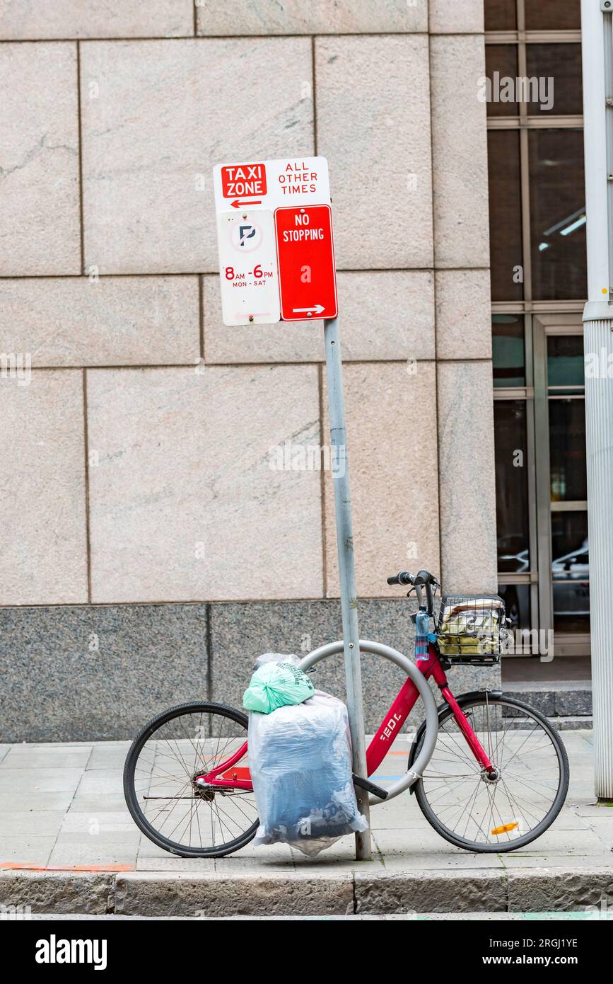 A red ex-hire bicycle with lots of plastic bags attached, chained to a red street sign in central Sydney, New South Wales, Australia Stock Photo
