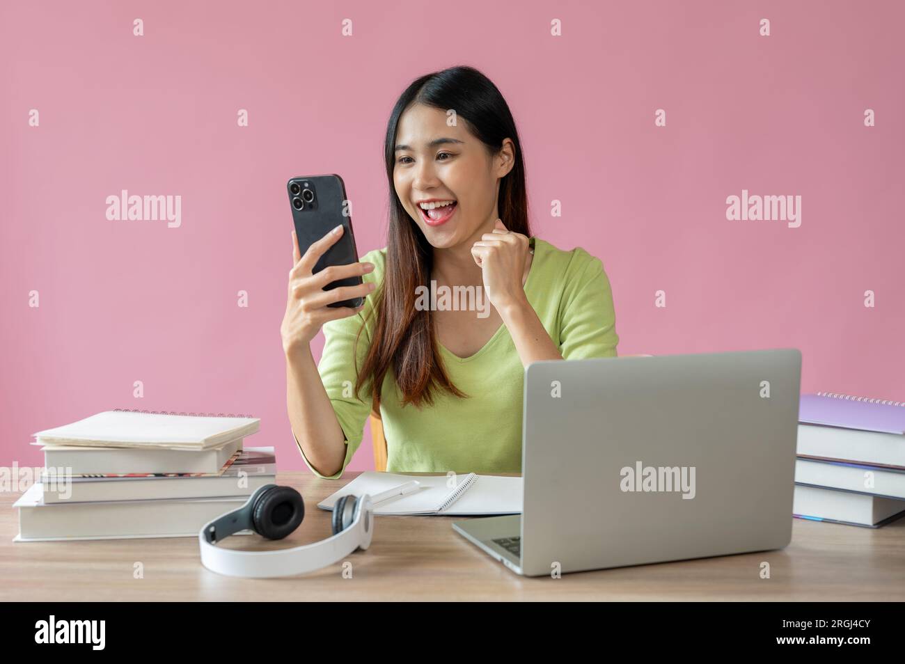 A beautiful and positive Asian girl is showing her fist and looking at her smartphone screen with a happy and excited face, receiving good news, passi Stock Photo