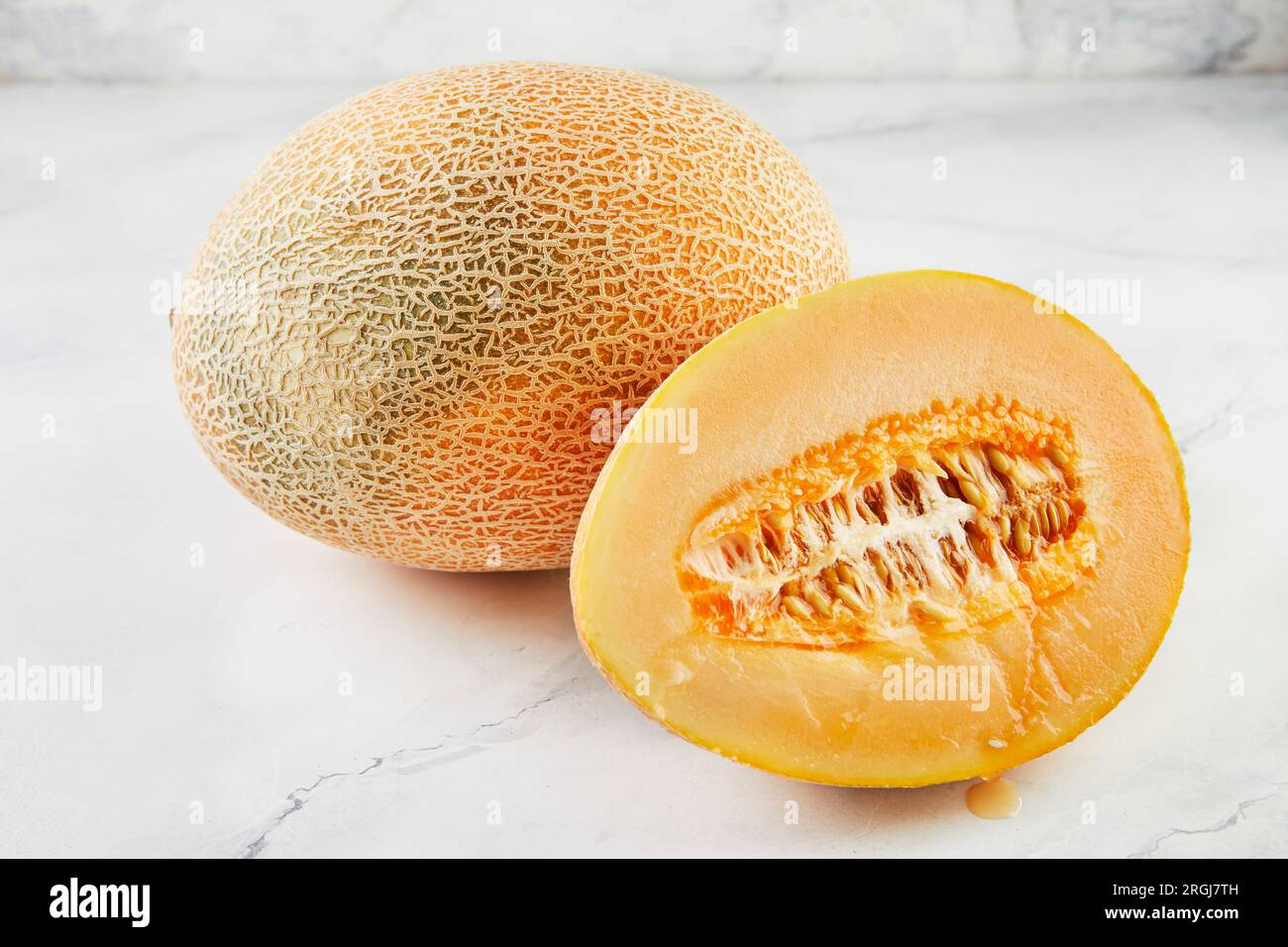 Two melons whole and half on light marble in home kitchen. Stock Photo