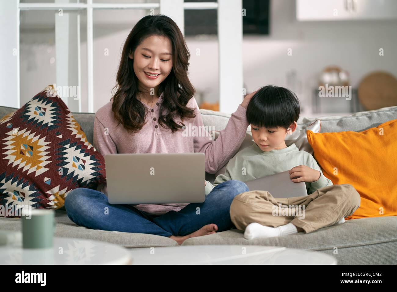 young asian mother and five-year-old son sitting on couch at home using laptop computer and digital tablet Stock Photo