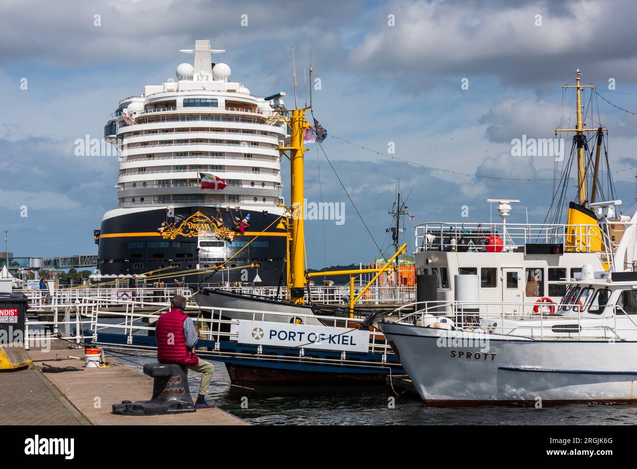 Kiel, Deutschland, August 2023 Hafenimpressionen Ein Angler auf einem Poller am Museumshafen  sitzend betrachtet die Disney Dream Stock Photo