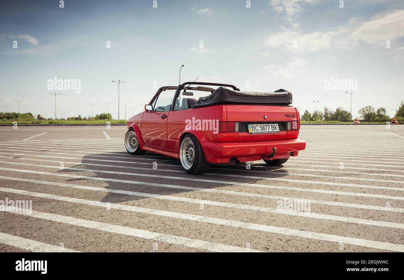 red Volkswagen Golf mk2 cabriolet on a big parking lot on a sunny day. Three quarter rear view of red car parked on striped asphalt surface. Stock Photo