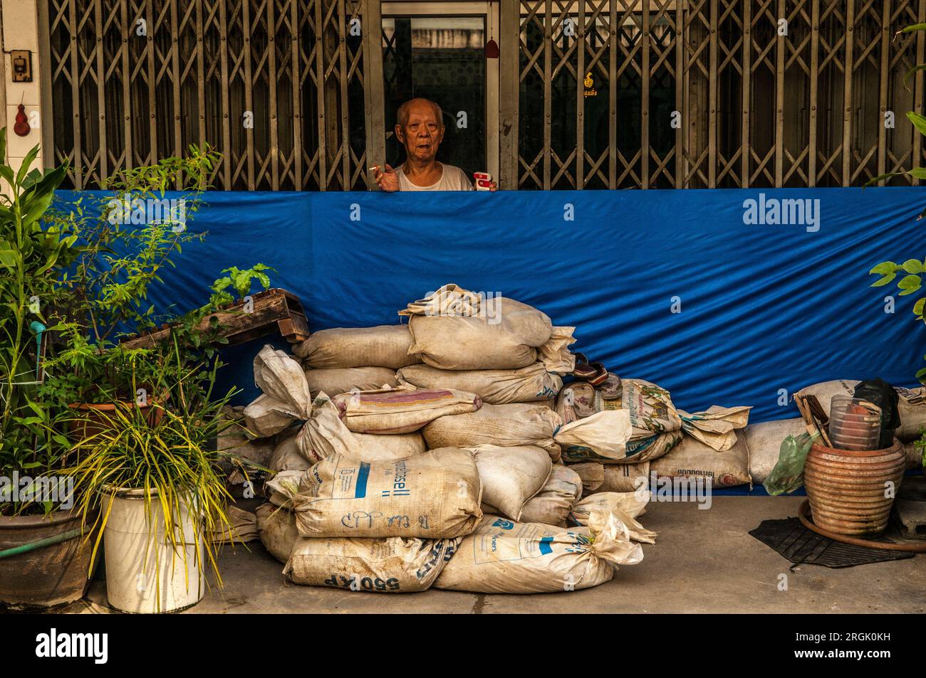 An elderly Bangkok resident prepares for the flood w/ sandbags in front of his shophouse, Sukhumvit Road, Bangkok, Thailand. credit: Kraig Lieb Stock Photo