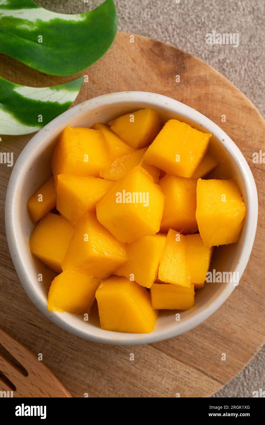Fresh chopped, diced mango cubes on gray table background with tropical leaf for eating. Stock Photo