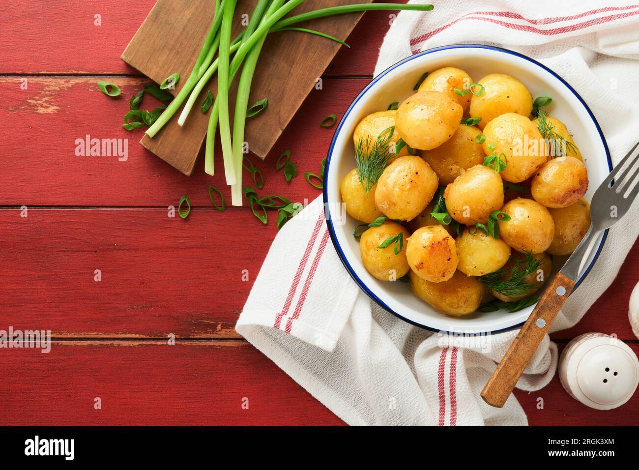 Fresh boiled new or young potatoes with butter, fresh dill and onions in white bowl on old red rustic wooden background. Tasty new boiled potatoes. To Stock Photo