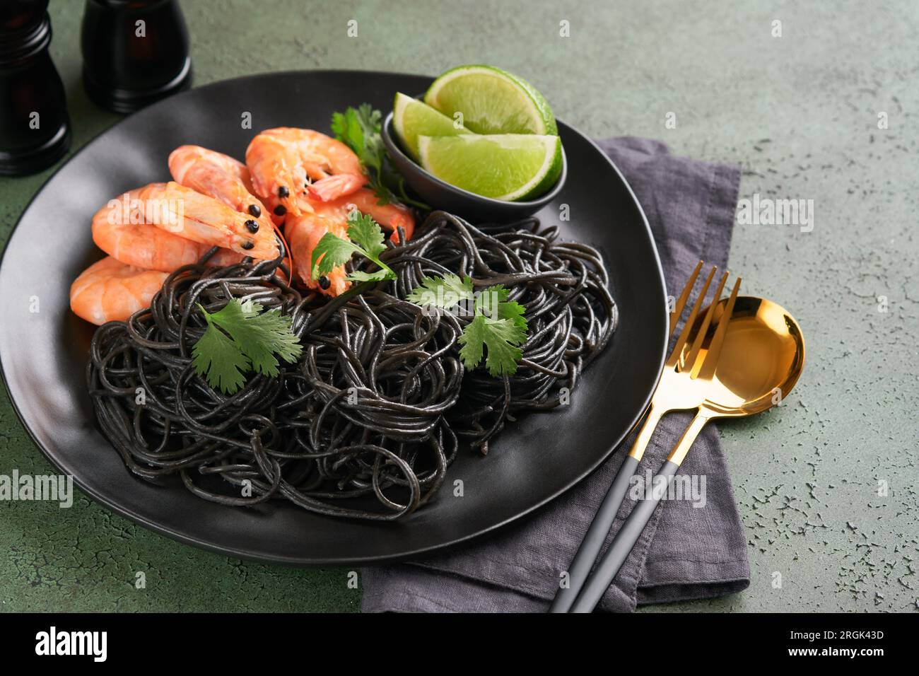 Black spaghetti pasta shrimp on black plate on dark concrete table background. Squid ink pasta with prawns. Pasta seafood. Top view on green stone tab Stock Photo
