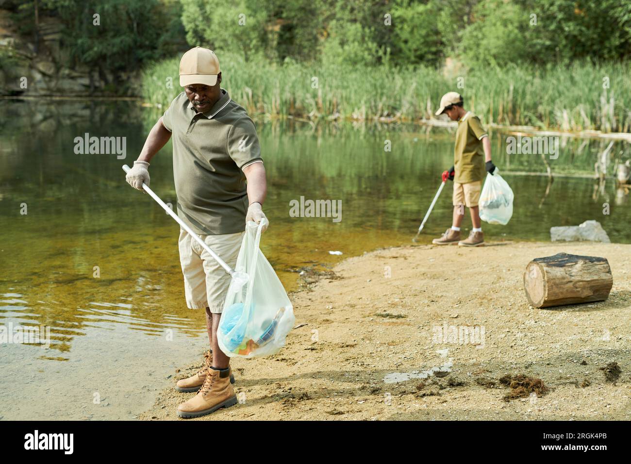 Dad cleaning the water from garbage together with his son outdoors Stock Photo