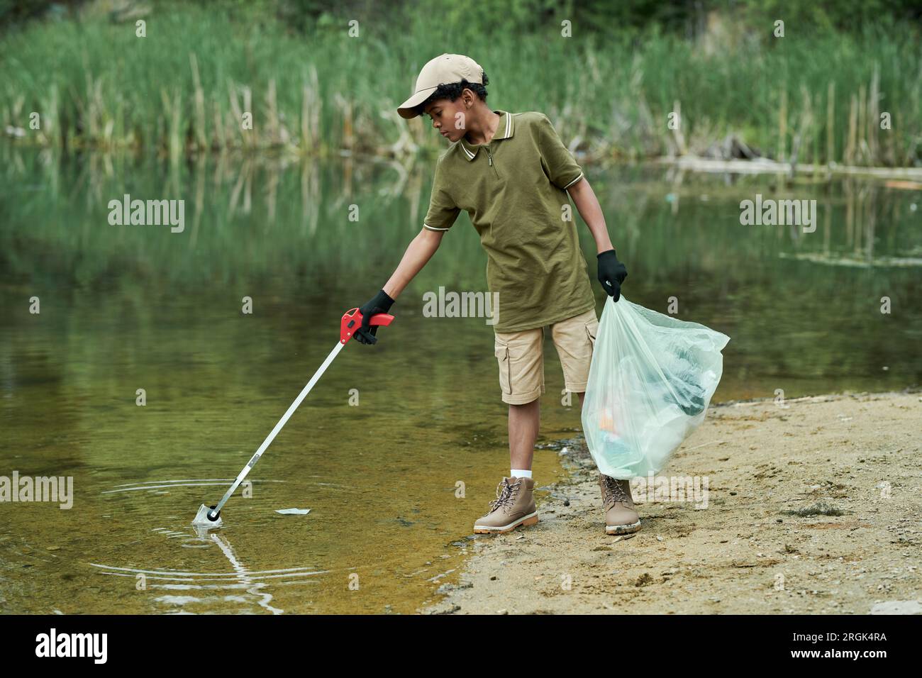 African American boy cleaning the lake from garbage with special stick Stock Photo