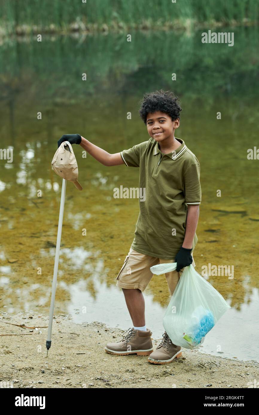 Vertical image of African American boy looking at camera while cleaning the lake from rubbish Stock Photo
