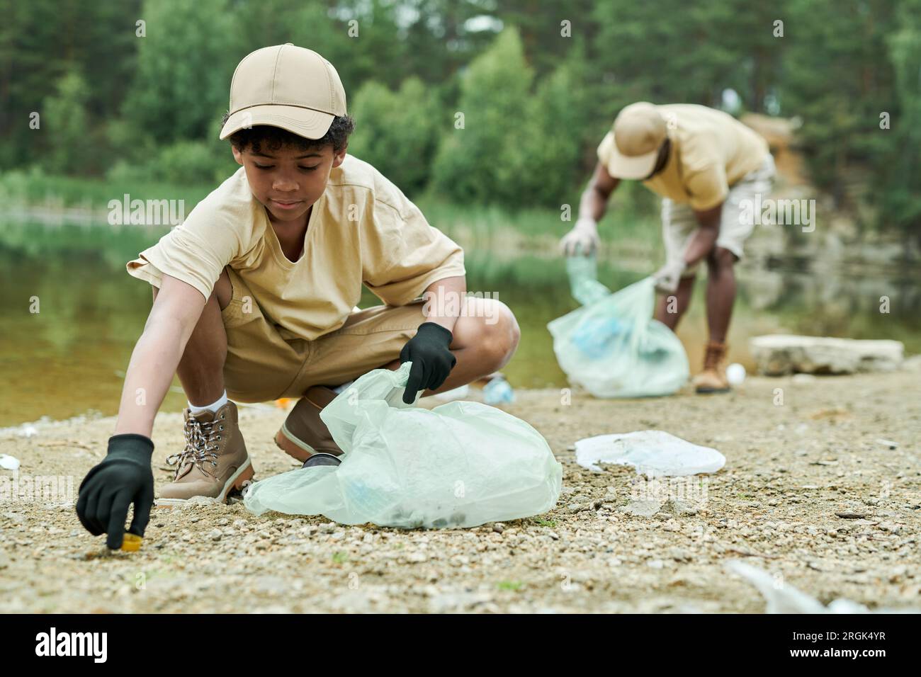 African American child cleaning territory around the lake together with his dad in background Stock Photo