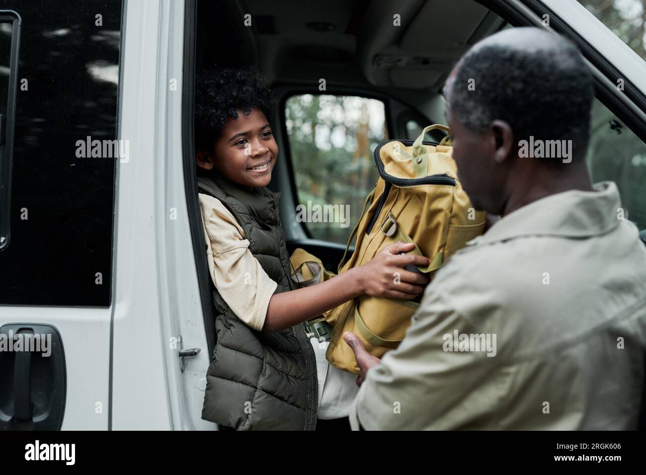 Little boy helping his dad to unloading bags from car for camping in the forest Stock Photo